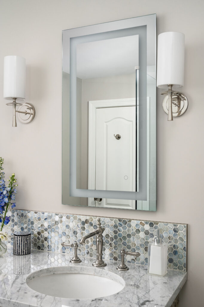 Marble-topped bathroom vanity with polished-nickel faucet, hexagon mosaic backsplash, lighted mirror above.