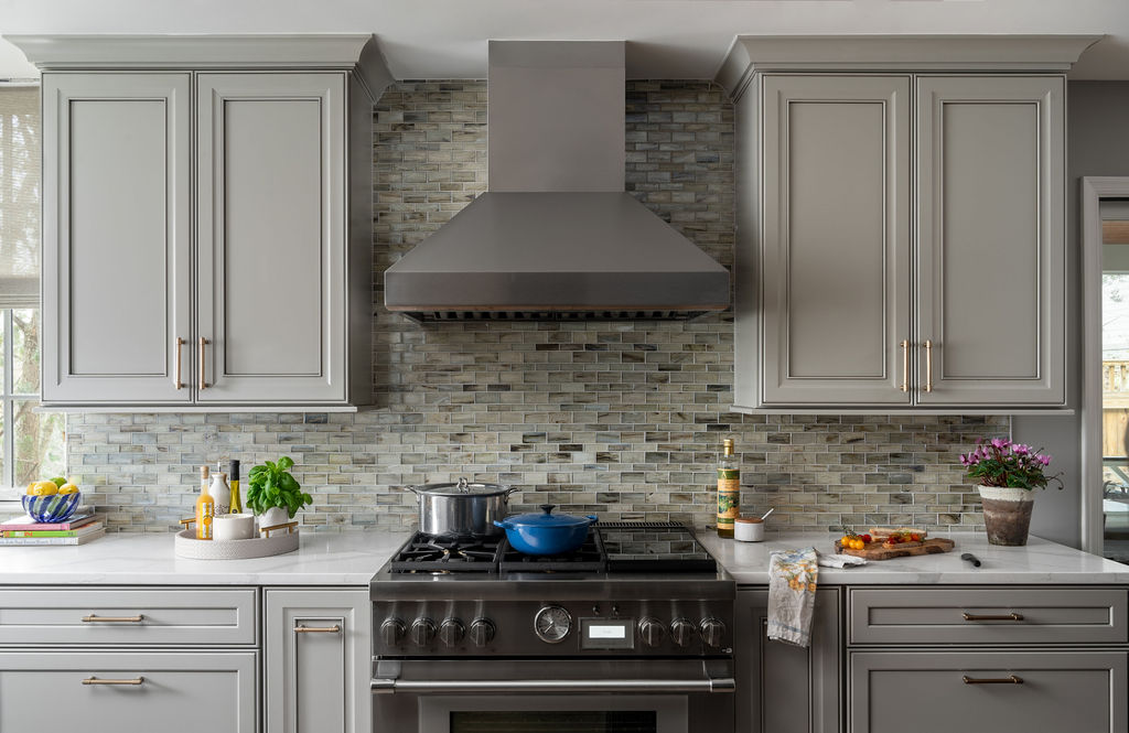 Kitchen range wall with stainless steel Thermador range, Zephyr hood, gray-painted cabinets, glass mosaic backsplash