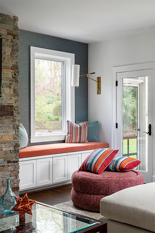 Reimagined fireplace reading nook, lined with metallic blue wallpaper, with mounted brass wall sconces and custom bench seat and colorful throw pillows
