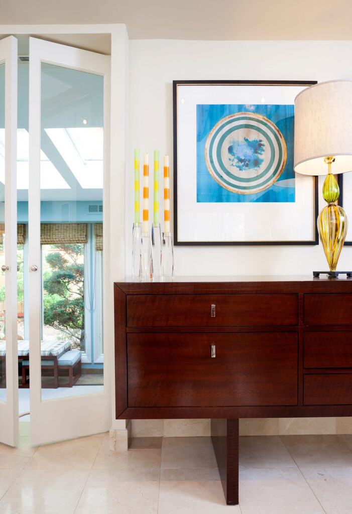 Modern interior featuring a wooden sideboard, colorful candles, framed art, and a stylish lamp in a bright space.