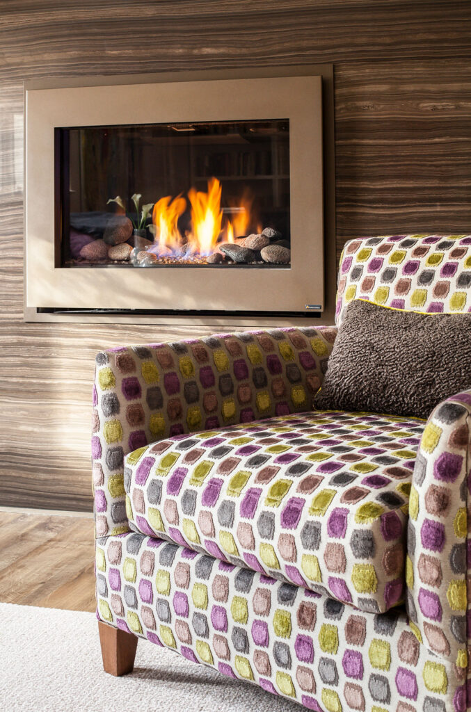 Cozy living room scene featuring a colorful patterned armchair and a modern gas fireplace with flames and decorative stones.