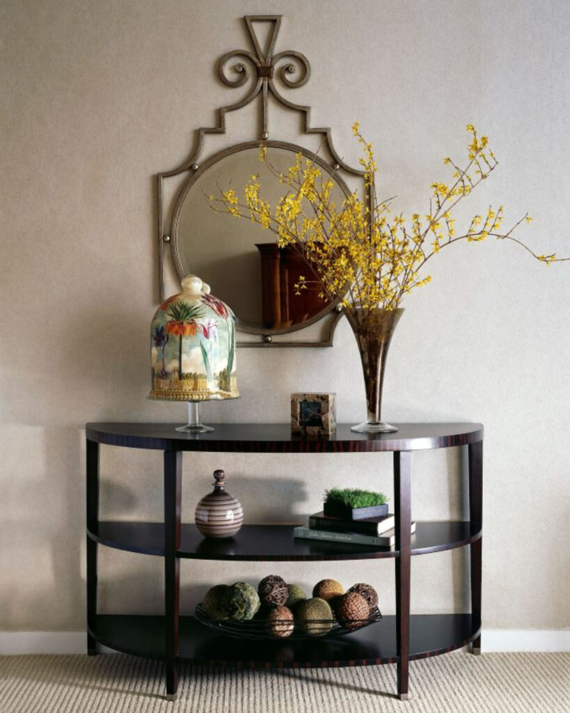 Elegant console table with decorative items, a mirror above, and yellow floral accents against a beige wall.