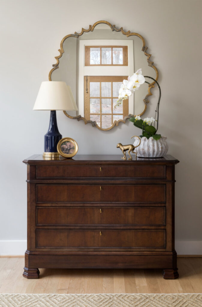 Elegant wood dresser with a mirror, lamp, and decorative plants, enhancing a stylish home interior design.