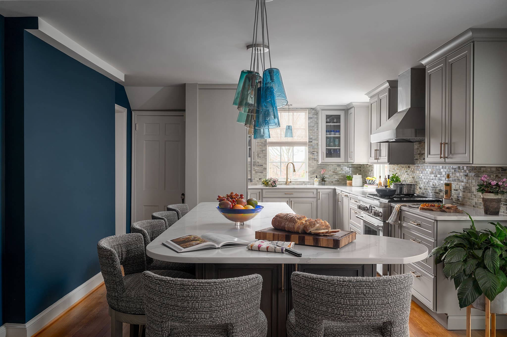 Renovated kitchen with L-shaped island, colorful glass pendant lights, and blue accent wall.