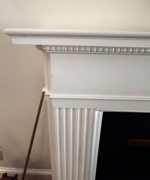 Close-up of a classic white fireplace mantel with detailed molding and fluted sides, enhancing interior decor.