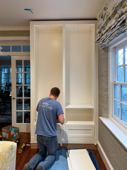 A carpenter installs a custom white built-in cabinet in a stylish home interior. Tools and materials are nearby.