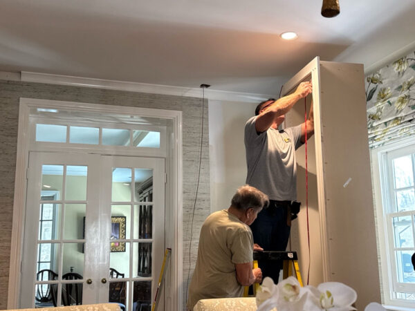 Two men installing cabinet in a bright, stylish room with French doors.