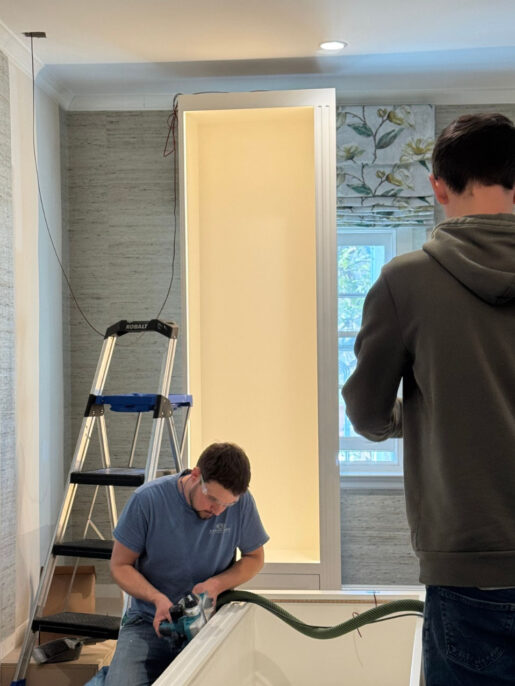Two workers are installing cabinetry in a bright kitchen, with tools and a ladder nearby for the renovation project.
