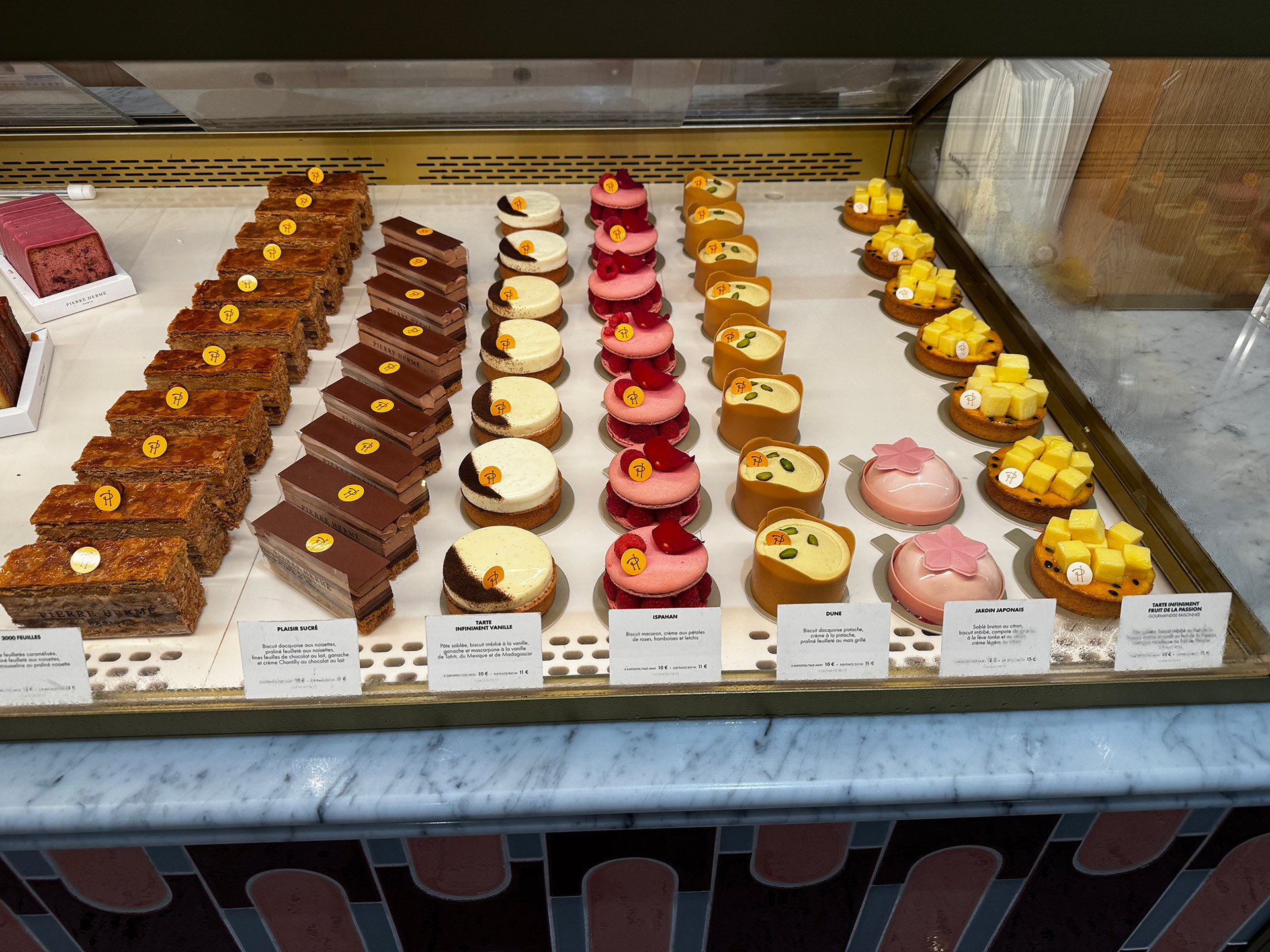 Colorful selection of gourmet pastries displayed in a bakery showcase, featuring various unique desserts and labels.