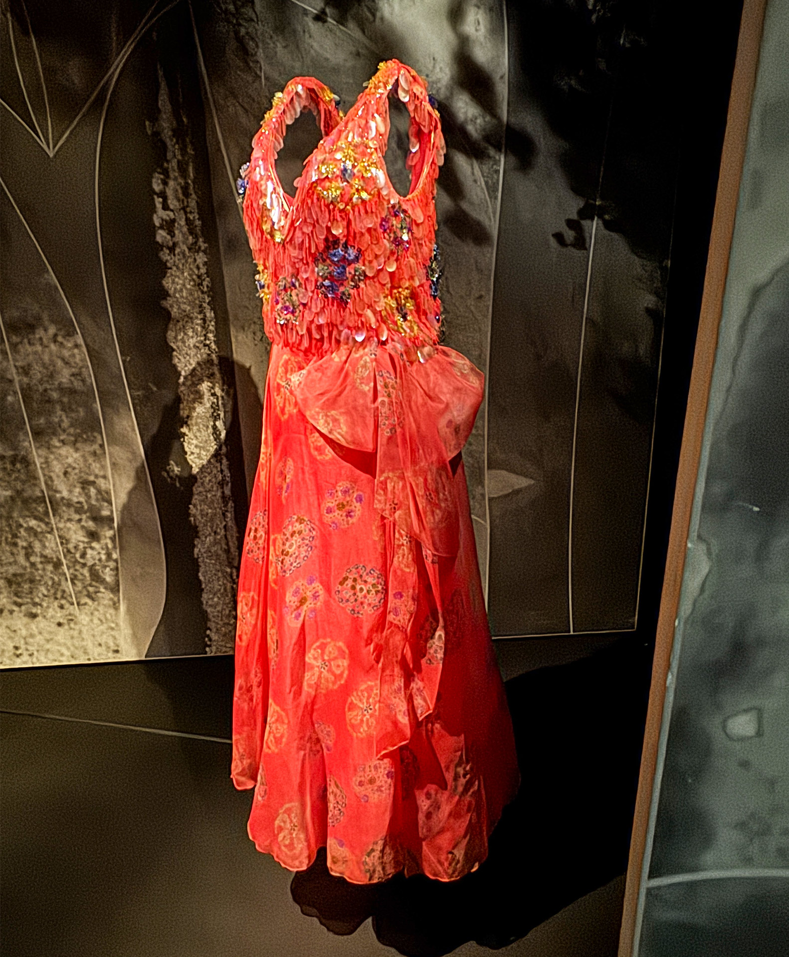 Vibrant red dress adorned with floral embellishments, displayed elegantly in a dimly lit exhibit.
