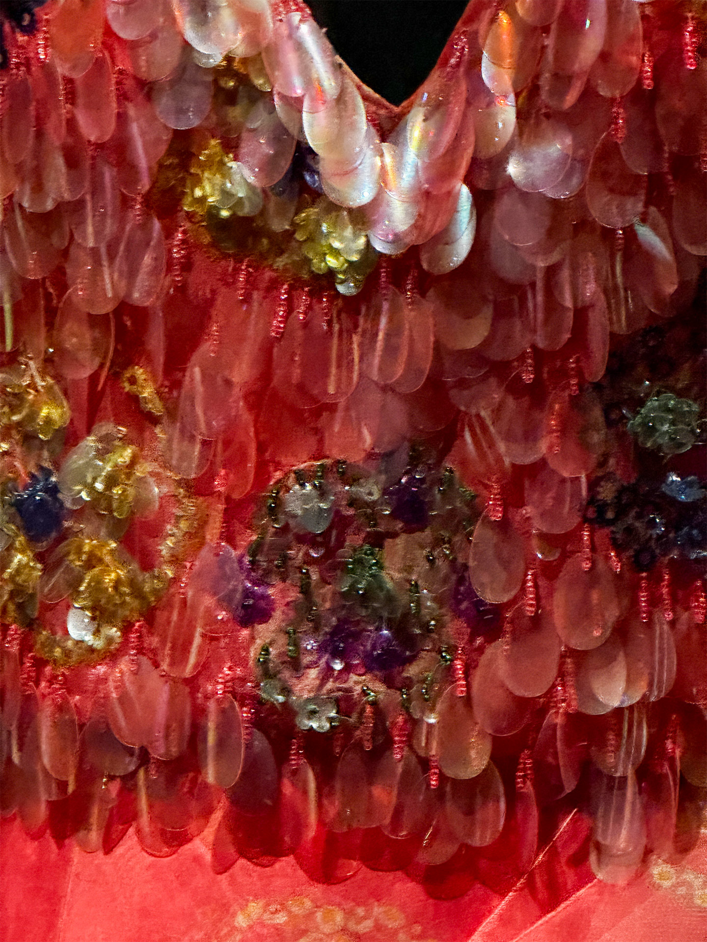 Close-up of a vibrant, textured red dress adorned with intricate, colorful beading and shimmering embellishments.