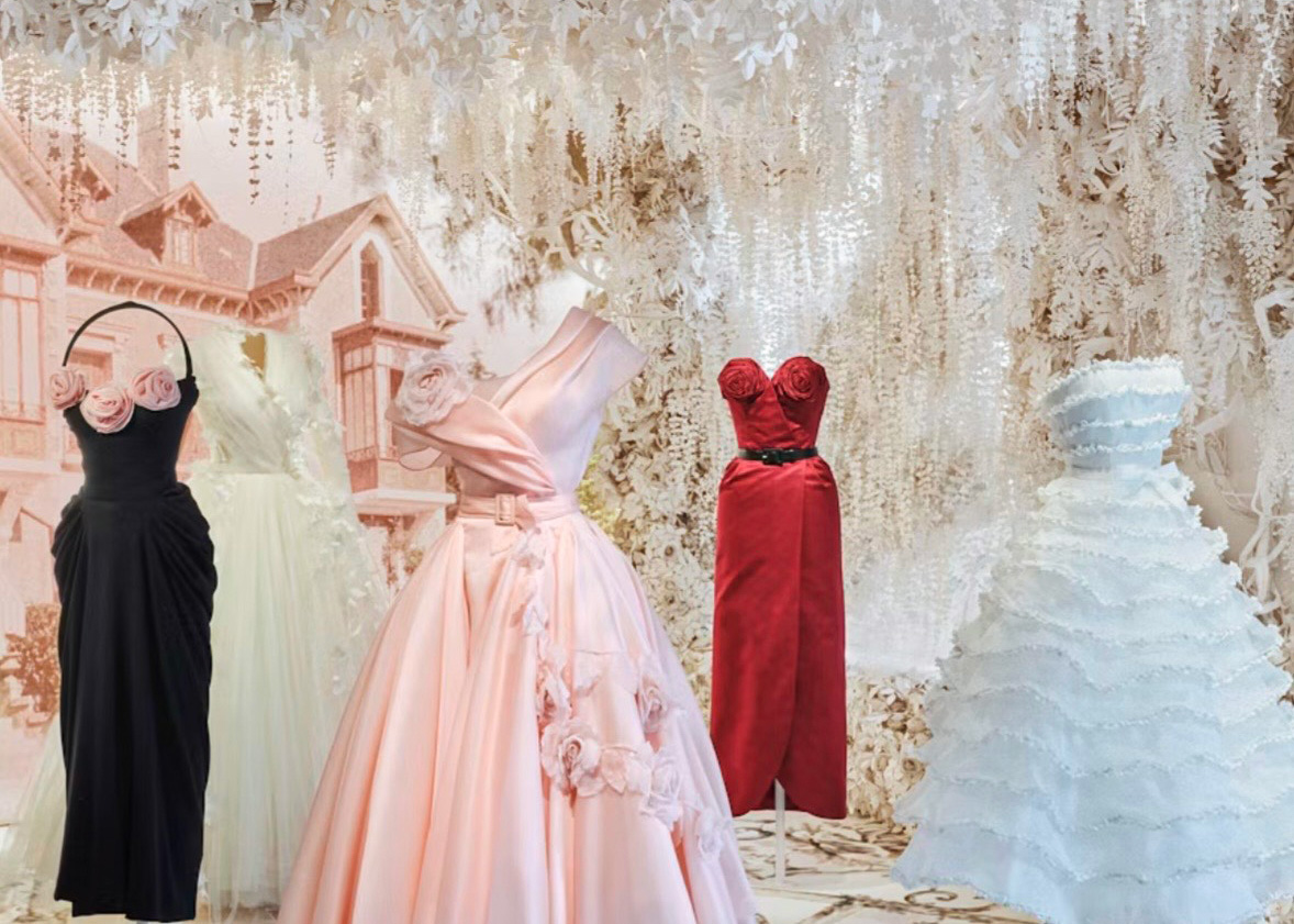 Elegant display of formal dresses in pastel colors, surrounded by floral decor in a stylish setting.