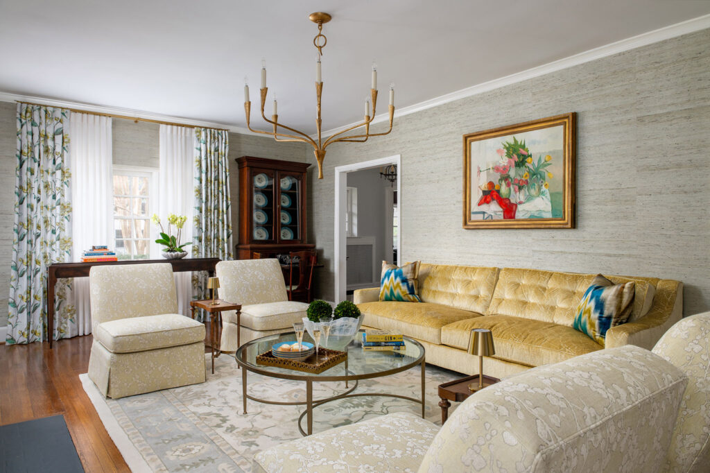 Elegant living room with a yellow tufted sofa, floral curtains, glass coffee table, and decorative artwork.