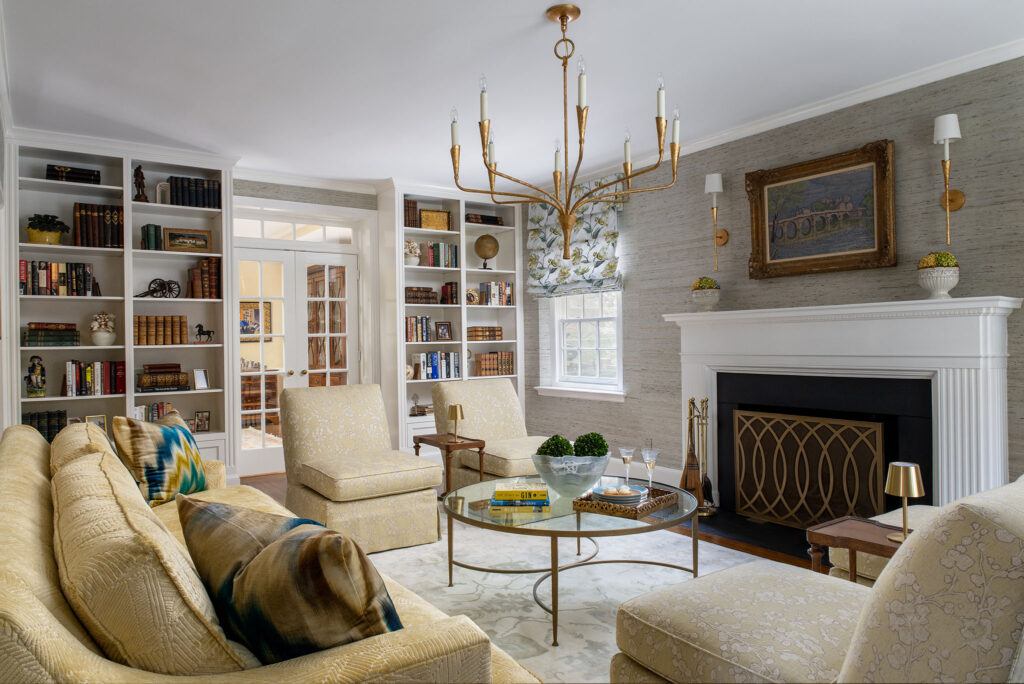 Elegant living room featuring plush seating, a glass coffee table, a modern chandelier, and built-in bookshelves.