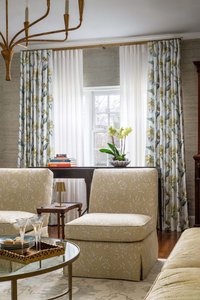 Bright living room featuring floral curtains, elegant furniture, and a vase of orchids by the window.
