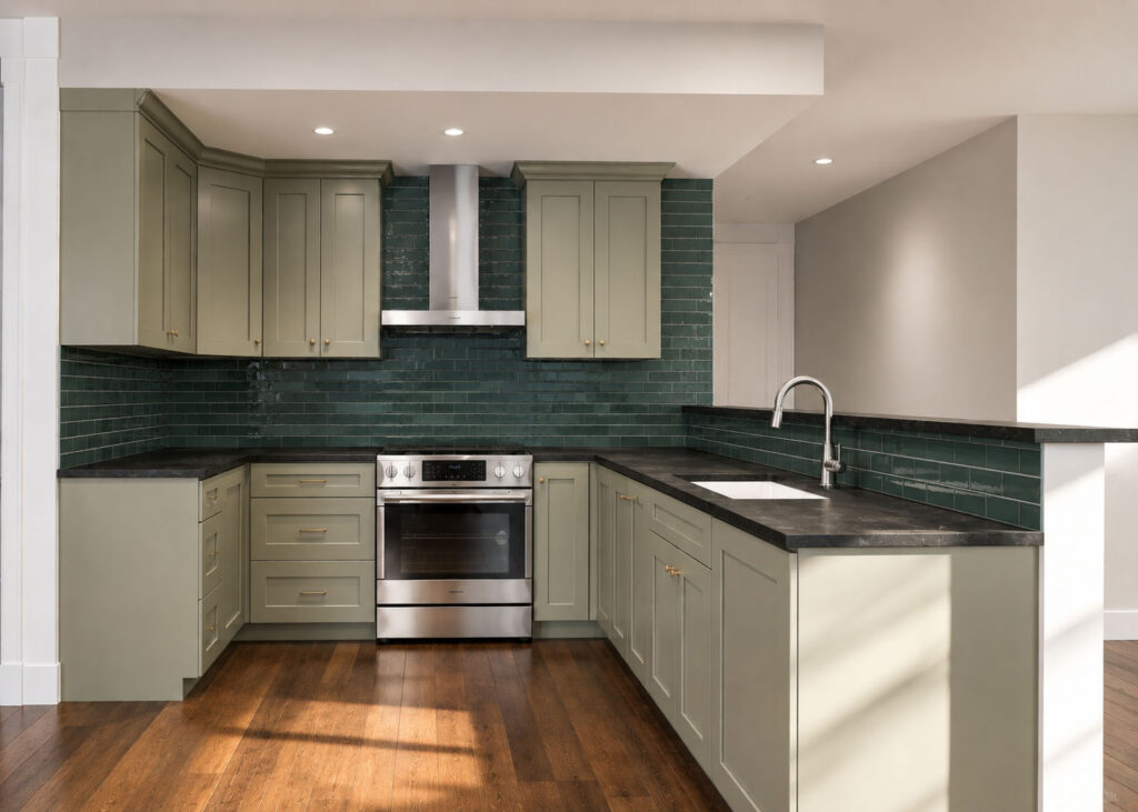 Modern kitchen with green cabinets, dark countertops, stainless steel appliances, and green tile backsplash.